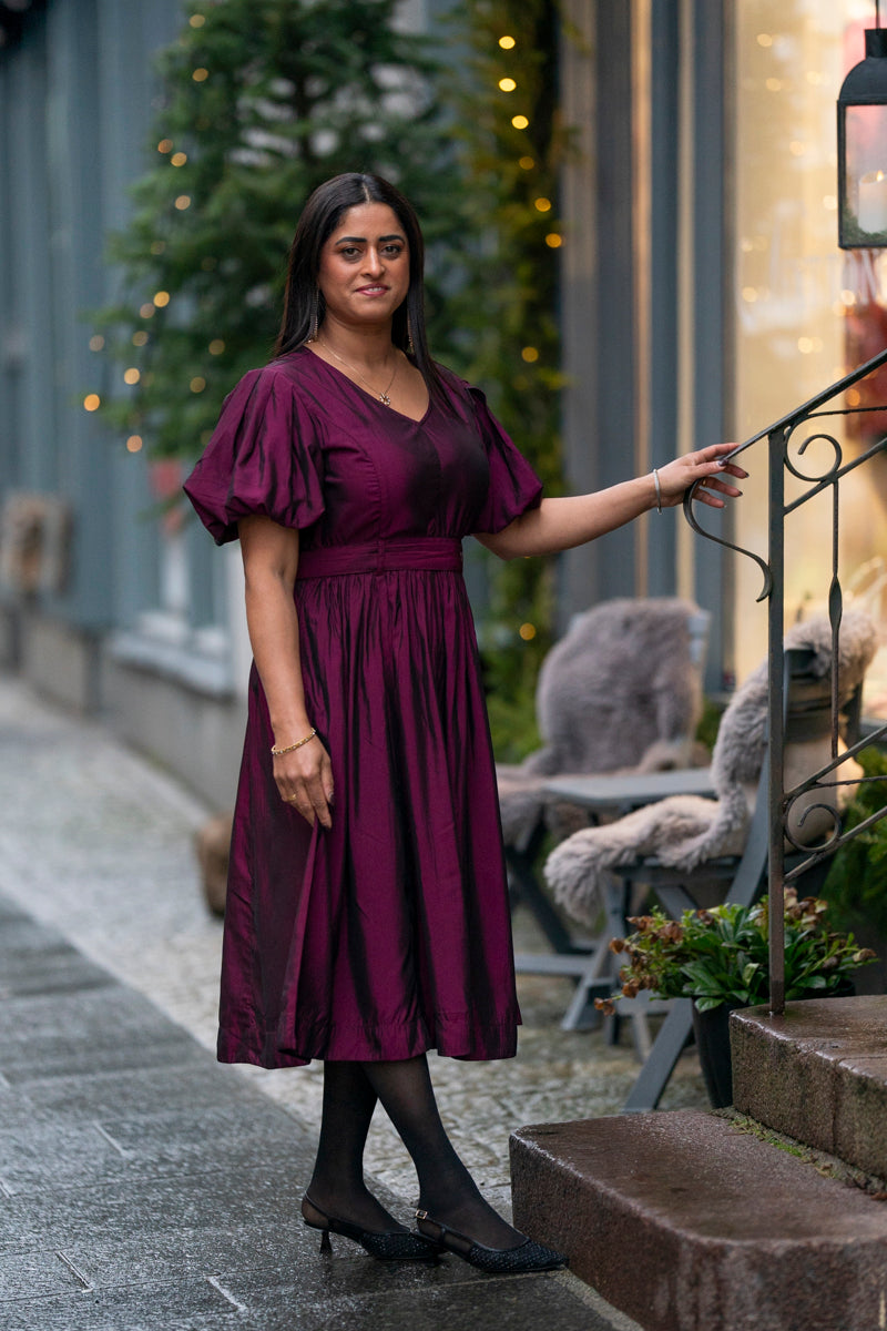 Vinrød kjole med puffermene, V-hals og elegant midi-lengde – perfekt til fest, bryllup og spesielle anledninger.