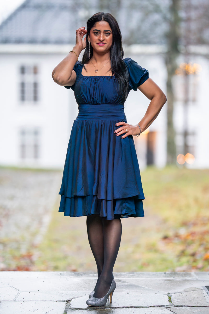 Marineblå kjole med lagdelt skjørt og elegant passform – perfekt til fest, bryllup og spesielle anledninger.